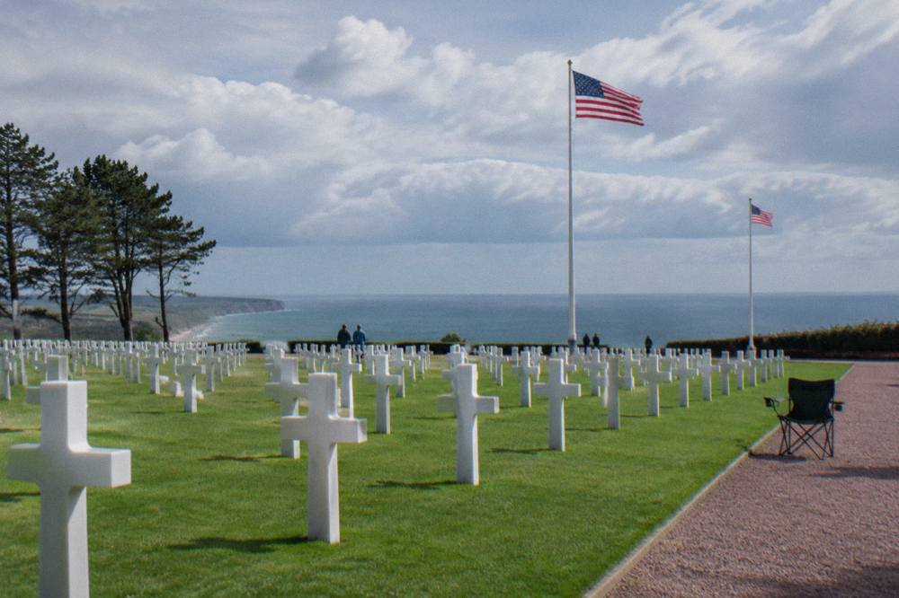 Flags flying beside rows of white crosses at a cliffside American war cemetery
