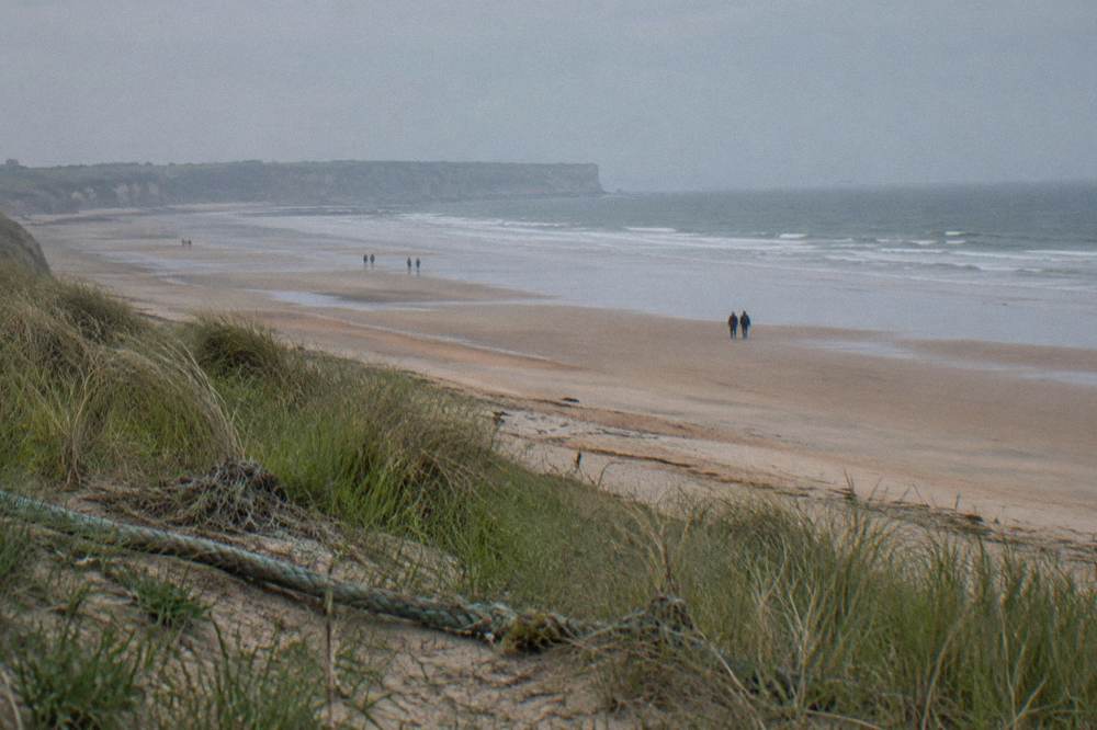 Wide sandy beach at low tide with gentle waves and distant cliffs