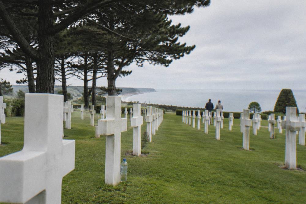 Rows of white crosses in a tree-lined military cemetery above the sea