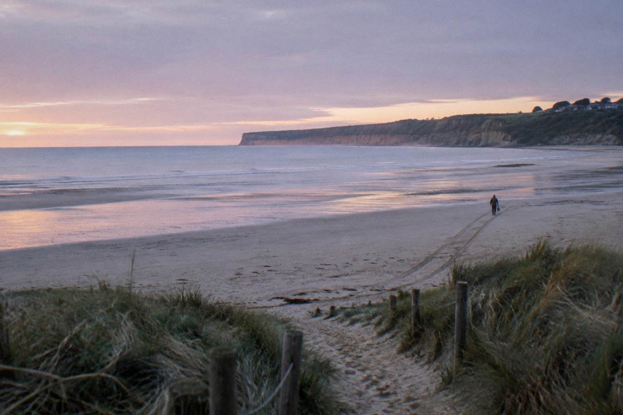 Wide sandy beach at low tide with grassy dunes and a quiet coastal road