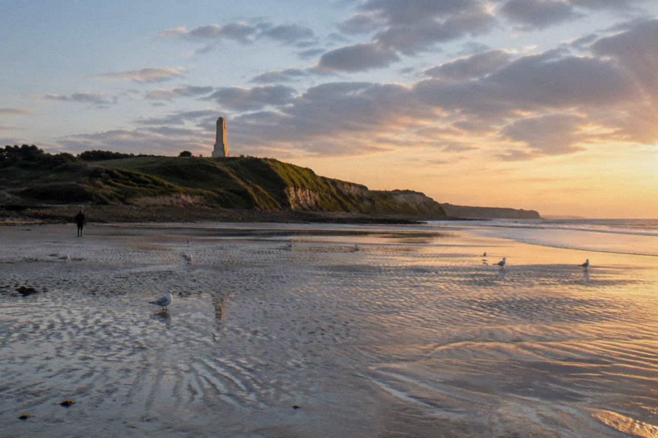 Wide view of Omaha Beach at low tide with the bluff and memorial visible beyond the sand