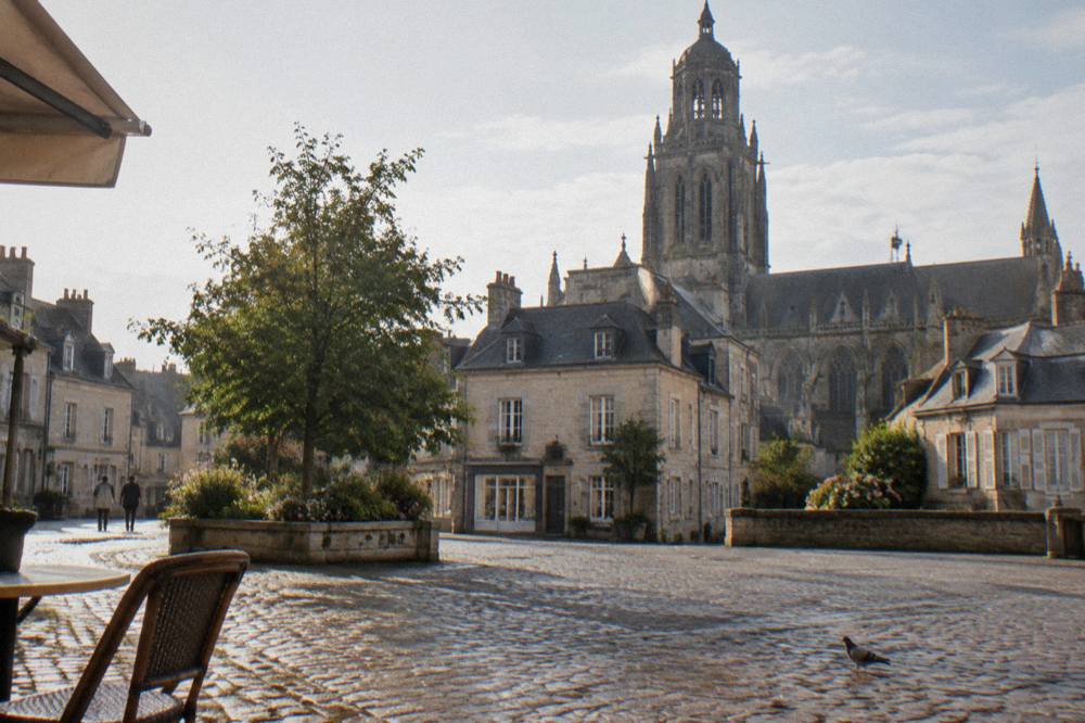 Cobblestone square with a stone church tower above small shops
