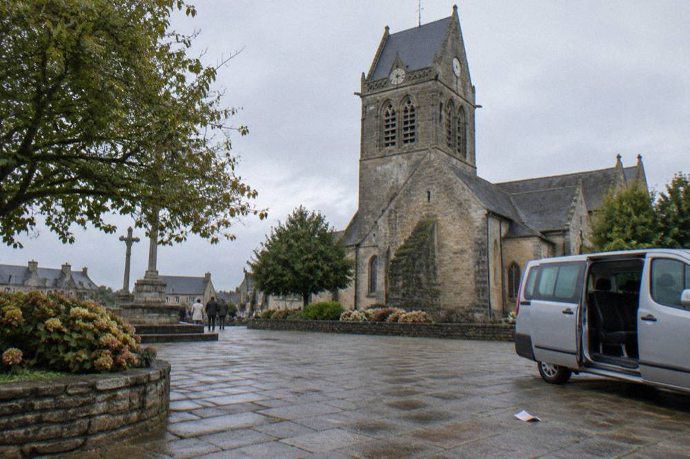 Minivan parked on a village square near a stone church in Normandy