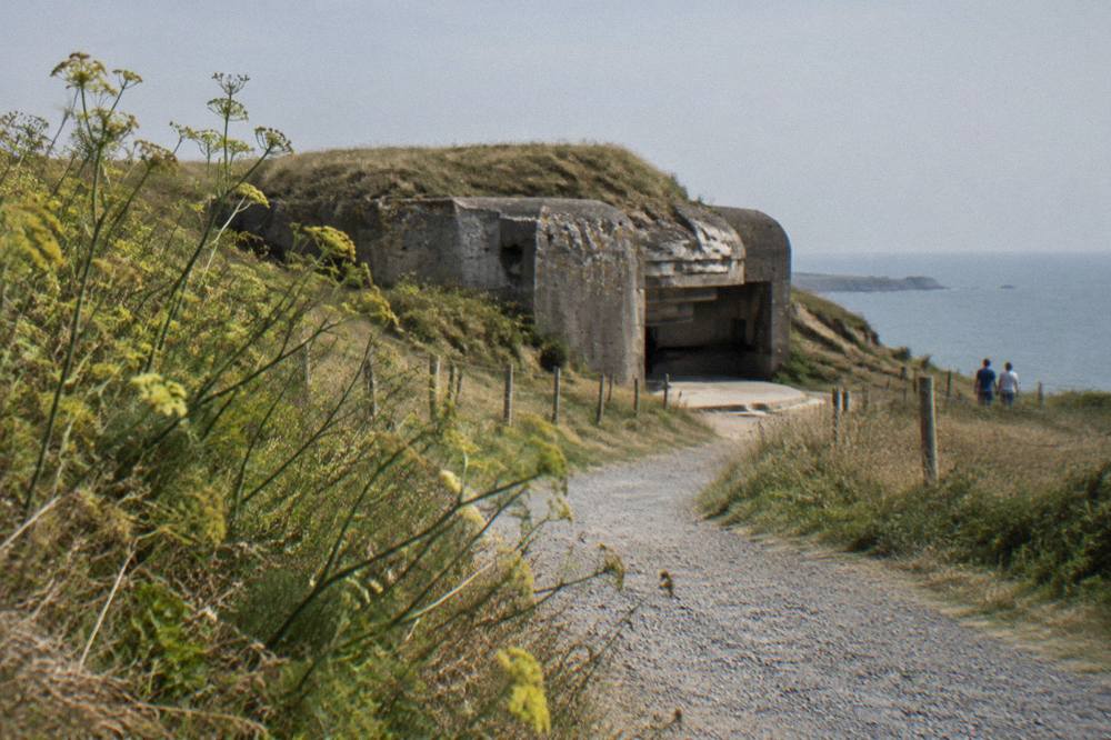 Grass-covered German bunker on a clifftop above the sea with a gravel path leading to it