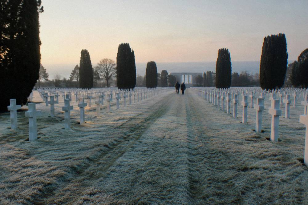 Rows of white headstones in alignment across a green lawn above the sea