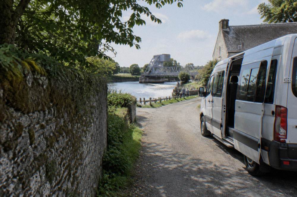 Small minibus parked on a narrow lane beside a stone wall near the coast