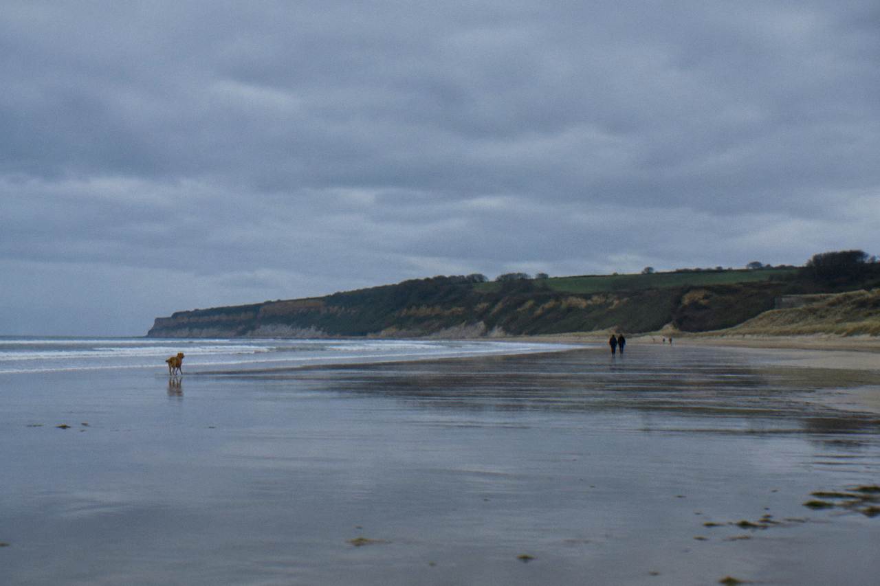 Wide view of Omaha Beach at low tide with flat sand and dunes under a gray sky