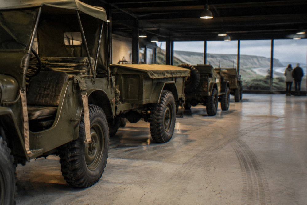 A row of restored World War Two military vehicles inside a dimly lit museum hall