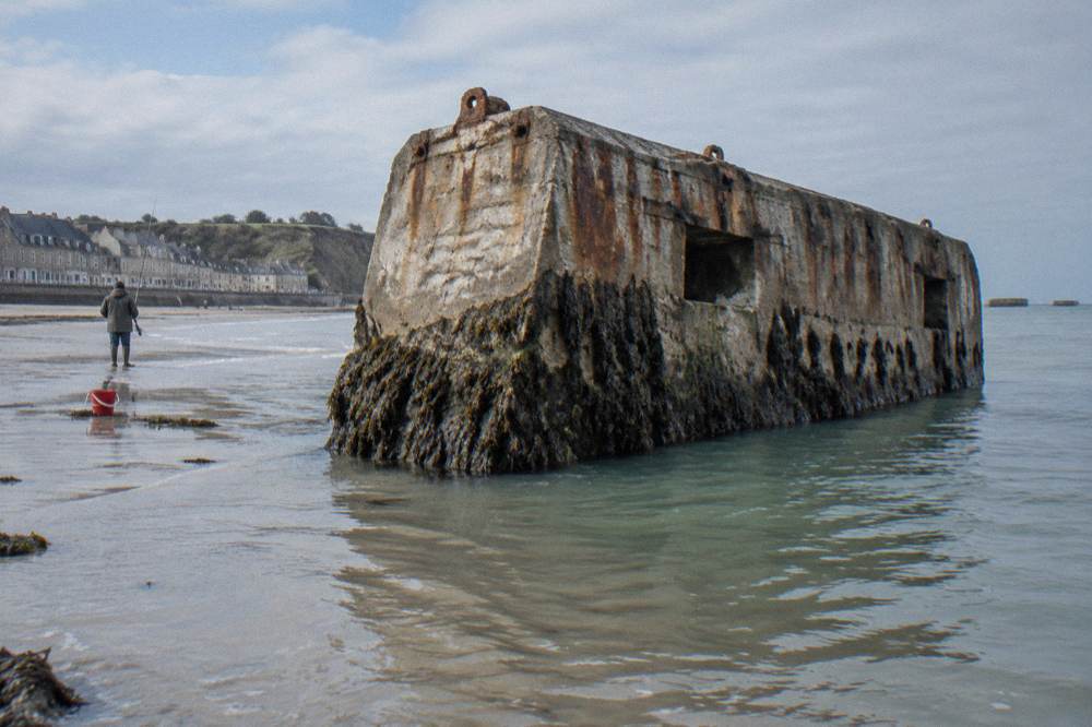Concrete harbour block standing in shallow seawater near a Norman town