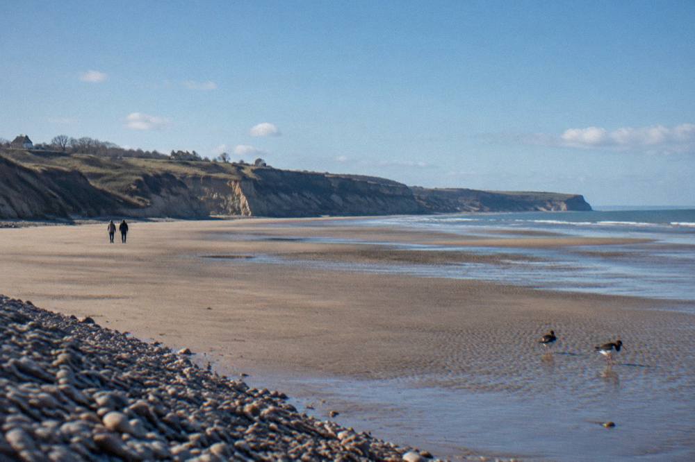 Wide sandy stretch of Omaha Beach at low tide with bluffs in the distance