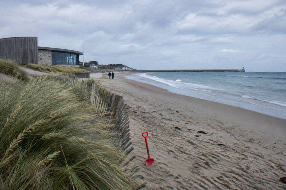 Quiet sand at Juno Beach with the shoreline curving toward Courseulles harbor