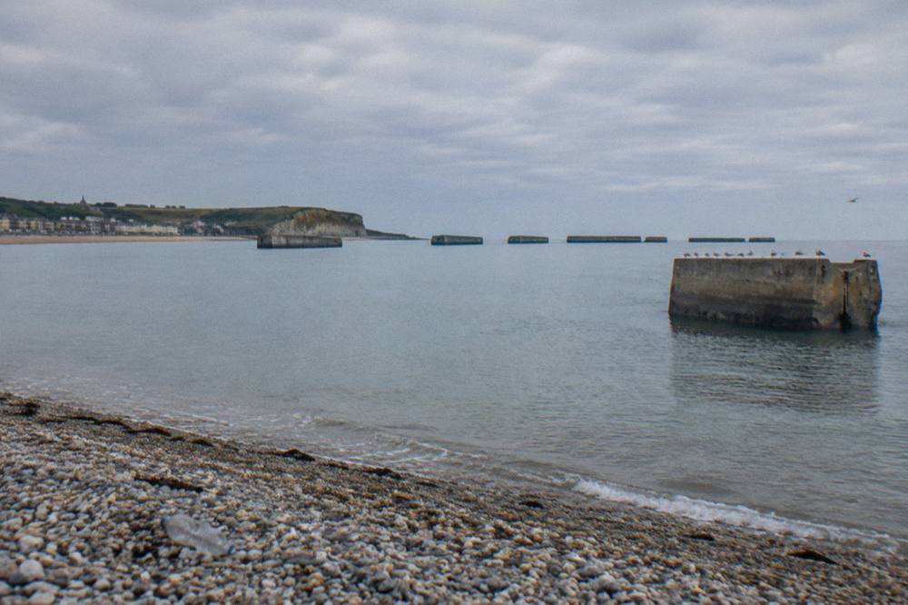 Remains of the artificial Mulberry harbor at Arromanches seen from the shore under a wide sky