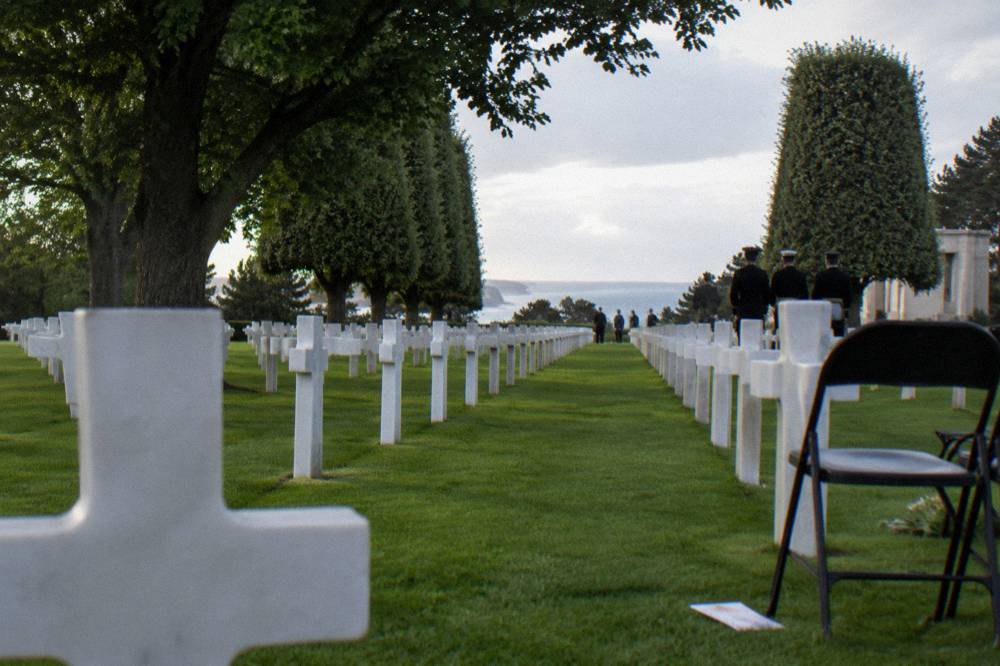 Rows of white marble headstones in the Normandy American Cemetery under tall trees