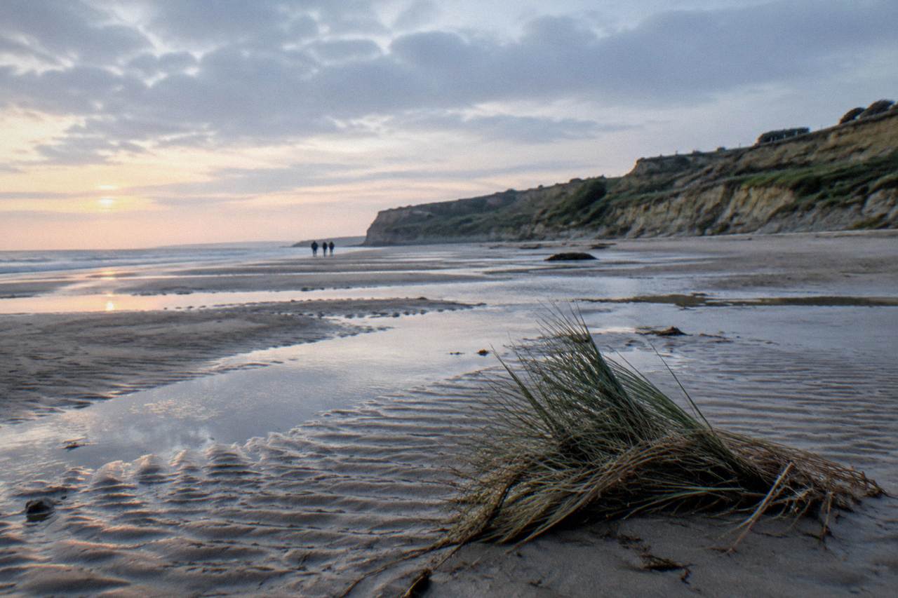 Wide view of Omaha Beach sand at low tide with the bluff and wartime terrain in the distance