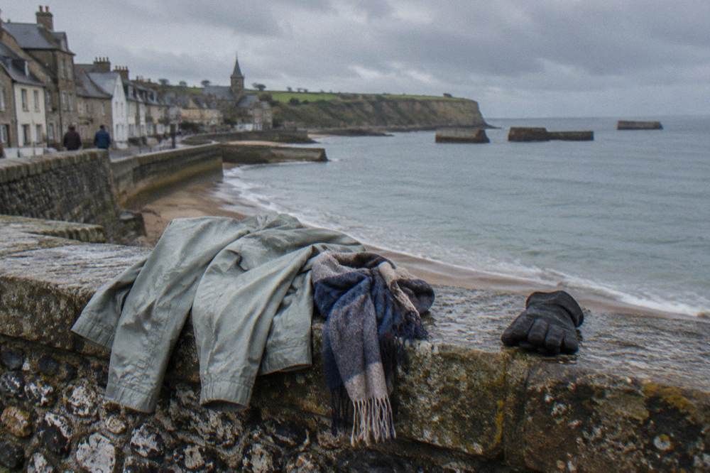 A light rain jacket and scarf draped over a bench beside a low stone wall overlooking a harbor