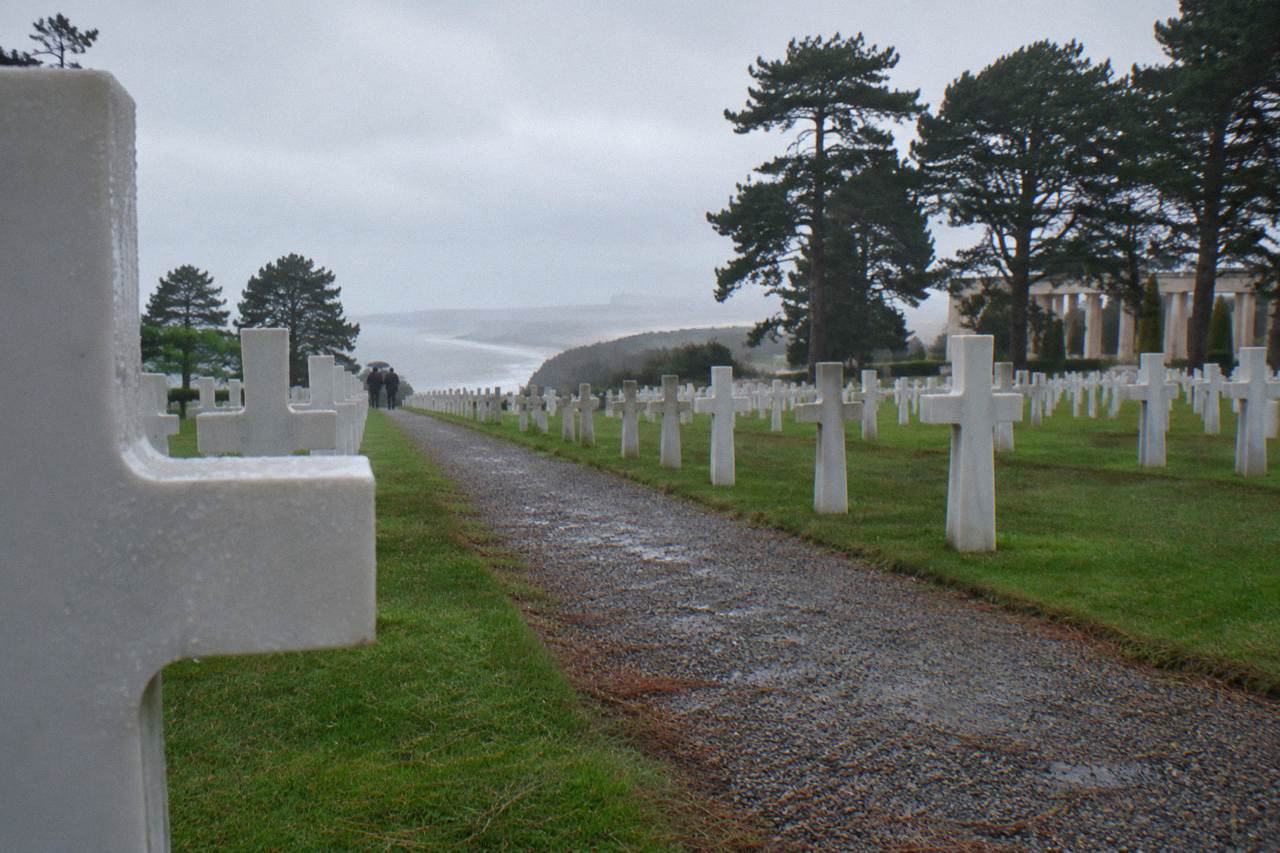A gravel path leading between rows of white headstones under a wide gray sky