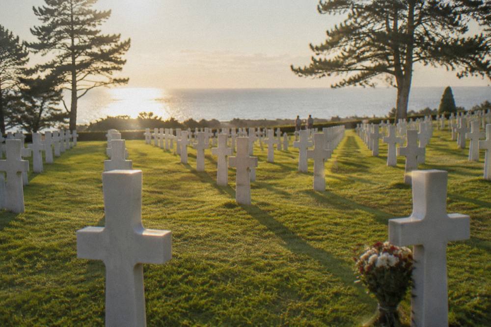 Rows of white crosses in a tree-lined military cemetery above the sea