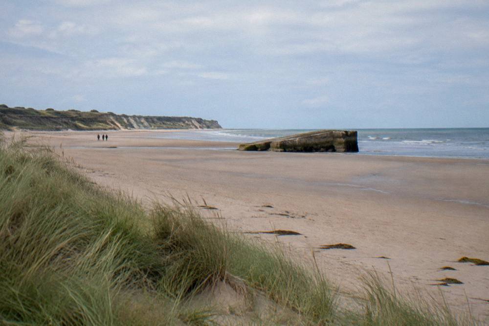Open sand and dunes at low tide with a distant concrete landing ramp