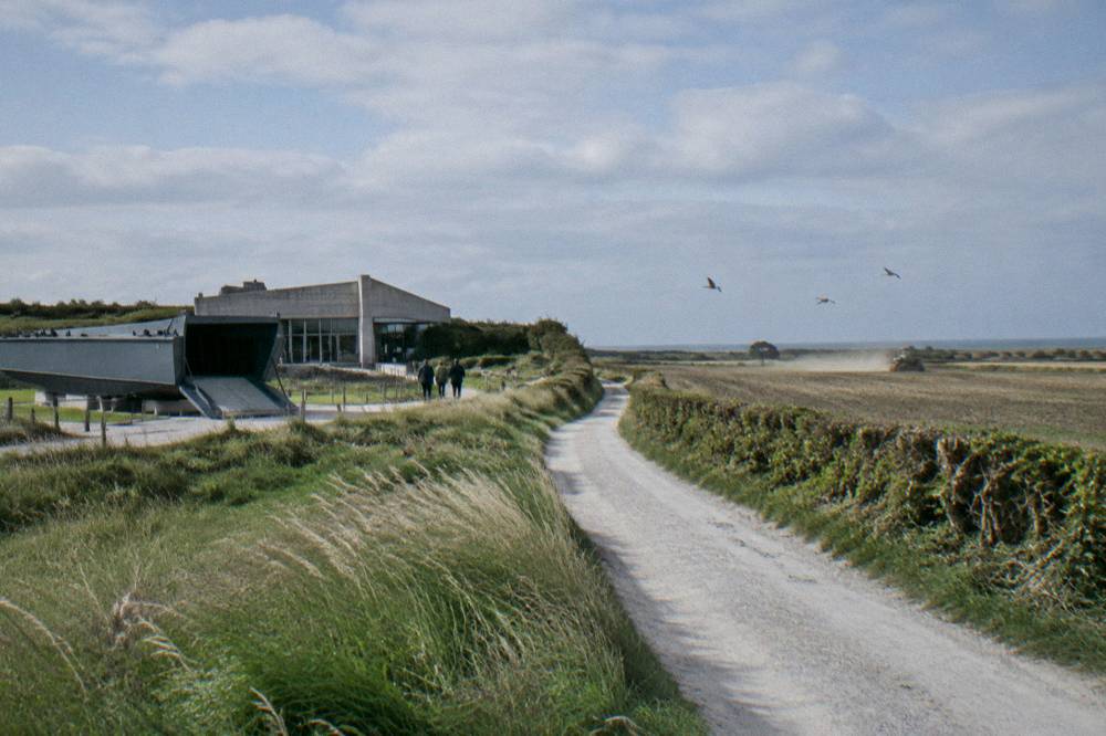 Open farmland and a narrow lane in the Utah Beach sector under a wide sky
