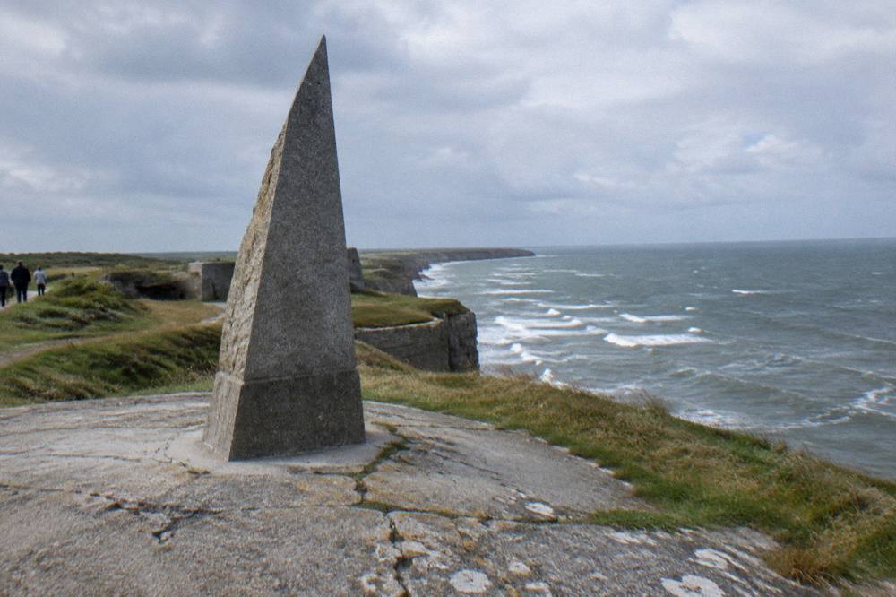 A clifftop landscape with wind-carved ground and a stone monument above the sea
