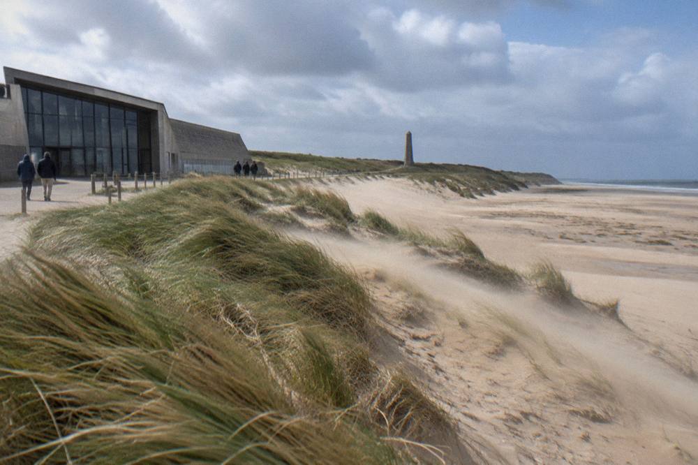 The wide flat sand of Utah Beach with dunes and a distant memorial sign