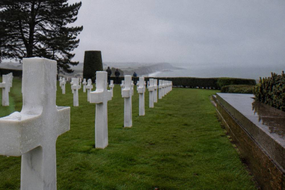 Rows of white grave markers on a green lawn above the sea