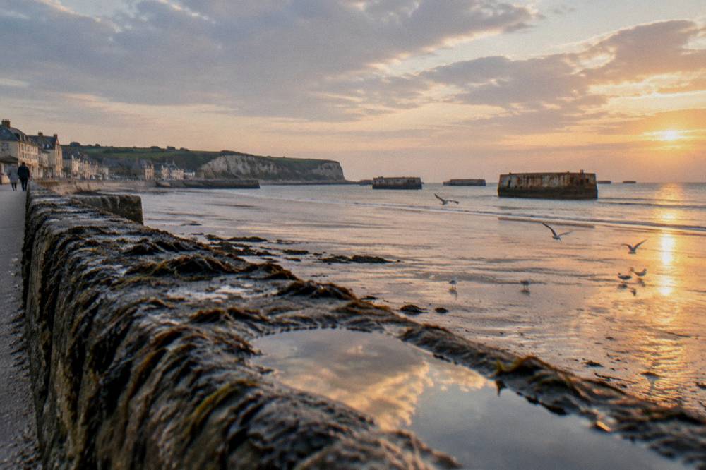 Autumn light over a stone harbour wall with wartime concrete remains beyond