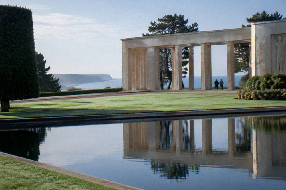 Reflecting pool and colonnade of a cliff-top cemetery in morning light