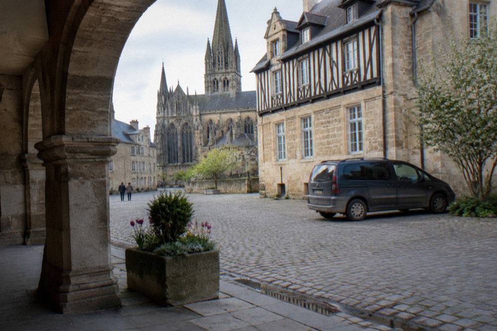 Minivan parked on a cobbled square beside stone buildings in a small French town