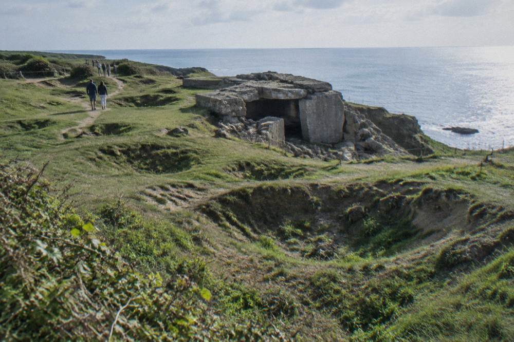 Blast cratered clifftop field with a broken concrete bunker and the sea beyond