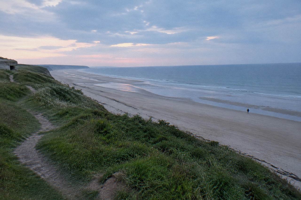 Wide view over the sandy stretch of Omaha Beach at low tide with grassy bluffs behind