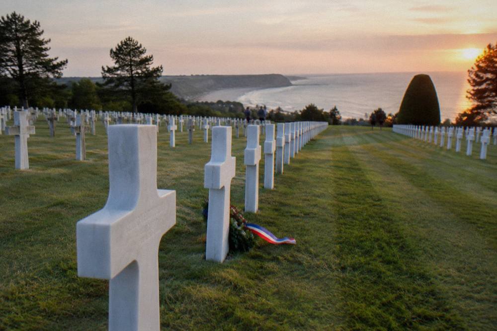White marble headstones in rows above the green lawn of the Normandy American Cemetery