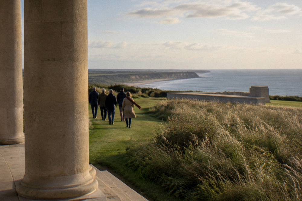 A guided group walking beside a stone memorial on a coastal path