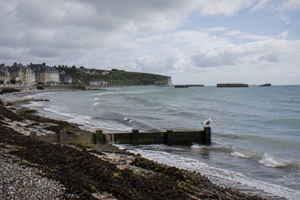 Wide flat sandy beach at low tide with gentle waves and dune grass along the top of the shore