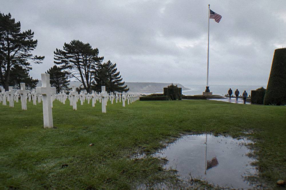 Rows of white marble headstones on a green lawn beside a tall flagpole