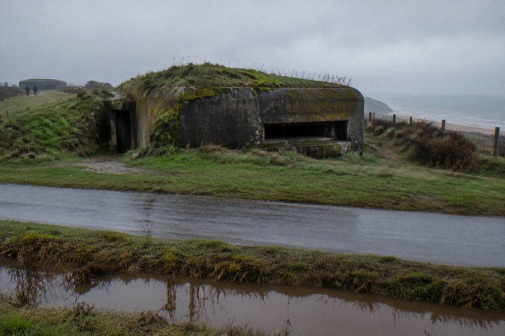 Low concrete bunker embedded in grassy ground near a quiet country road