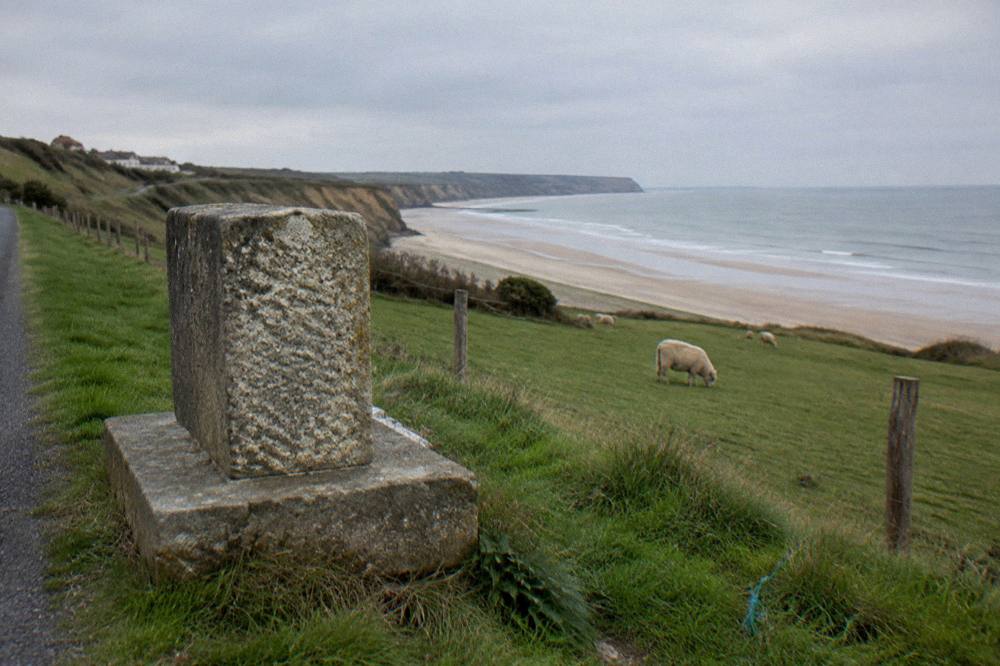 Quiet stone memorial beside a coastal road with fields and sea beyond
