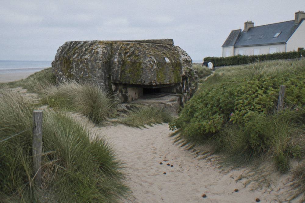 Concrete bunker remains on the dune line at Juno Beach beside a sandy path leading toward the sea