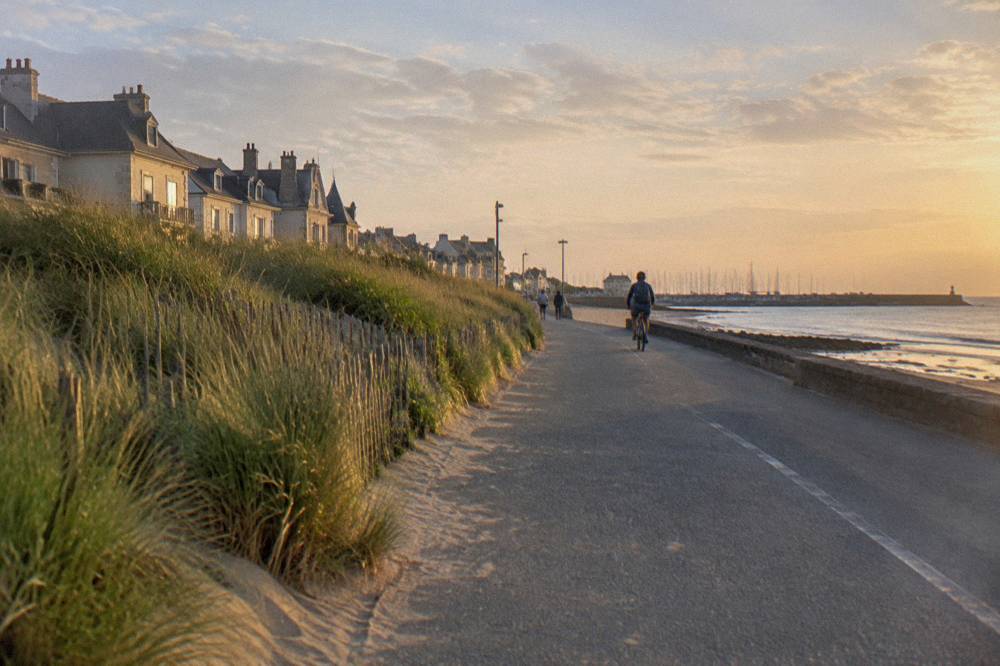 Coastal cycling path beside green fields running toward the harbor at Courseulles-sur-Mer