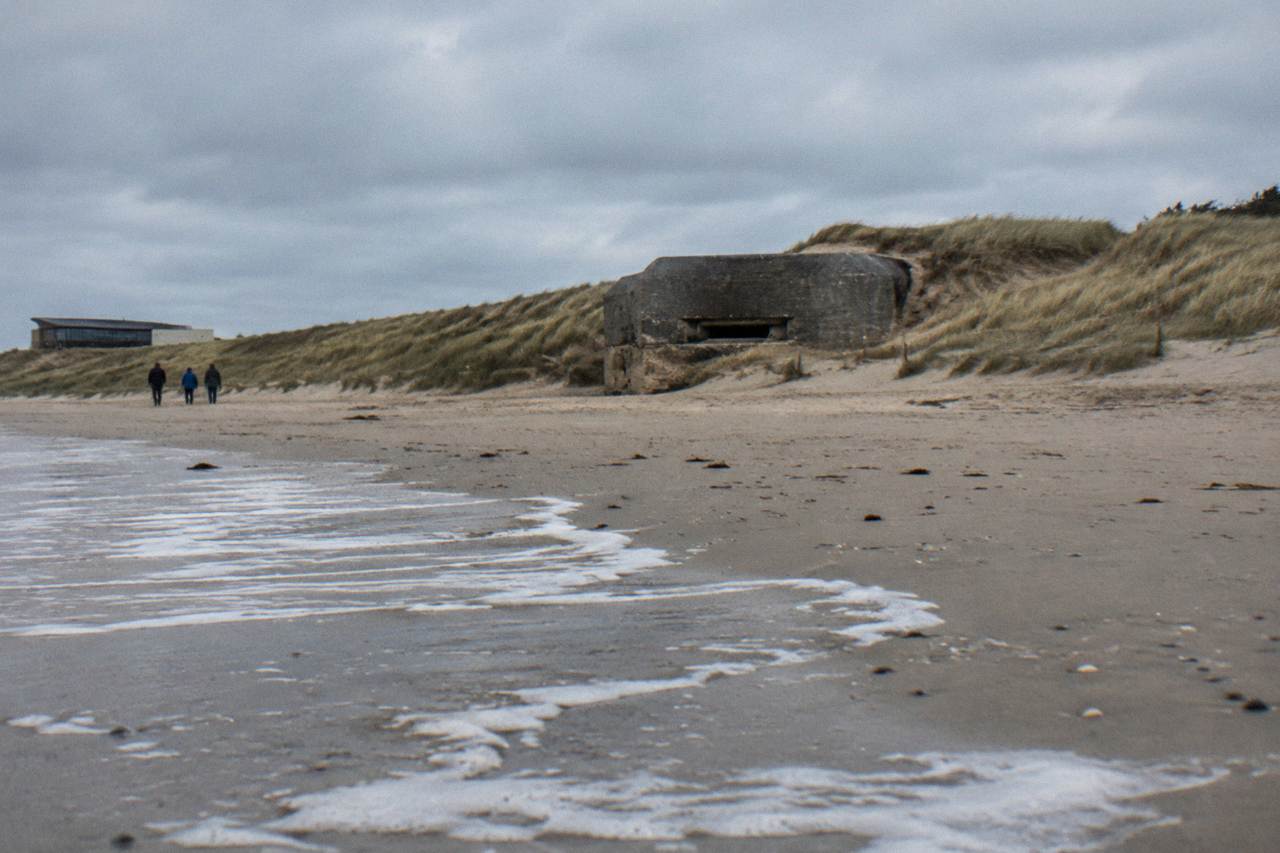 Wide sandy beach at Juno Beach with remaining wartime concrete structures near the dune line under a gray sky