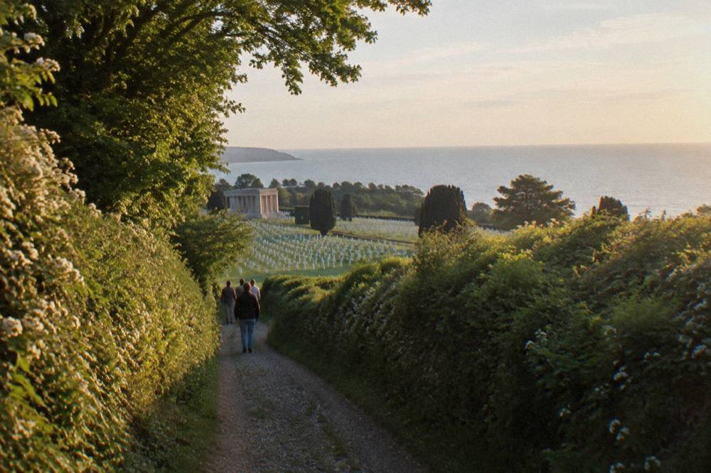 A country road winding through hedgerows toward the Normandy coast