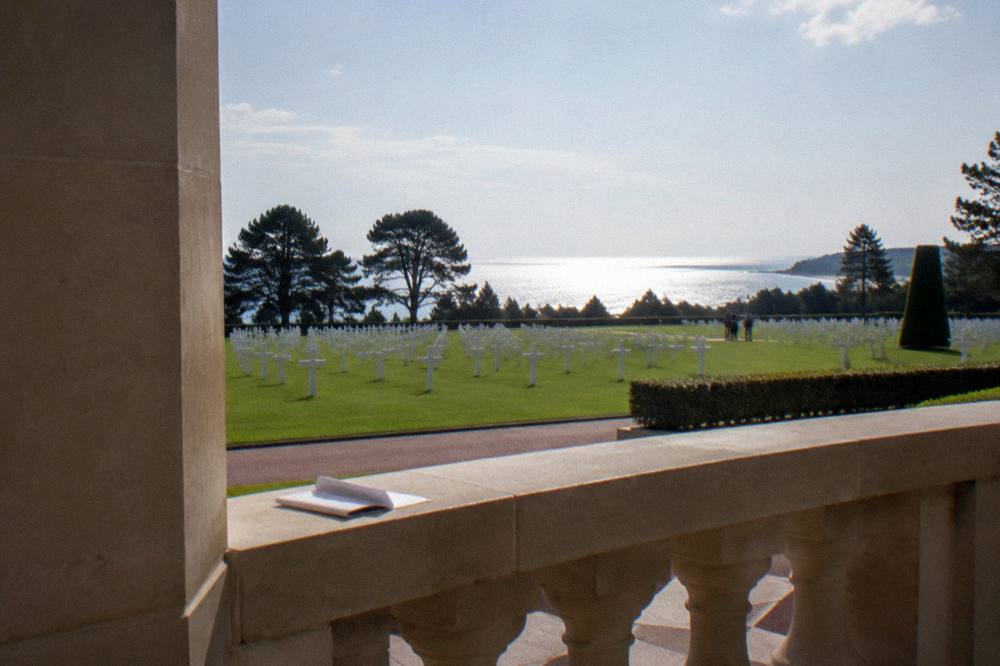 A colonnade of stone pillars standing above a wide lawn toward the sea