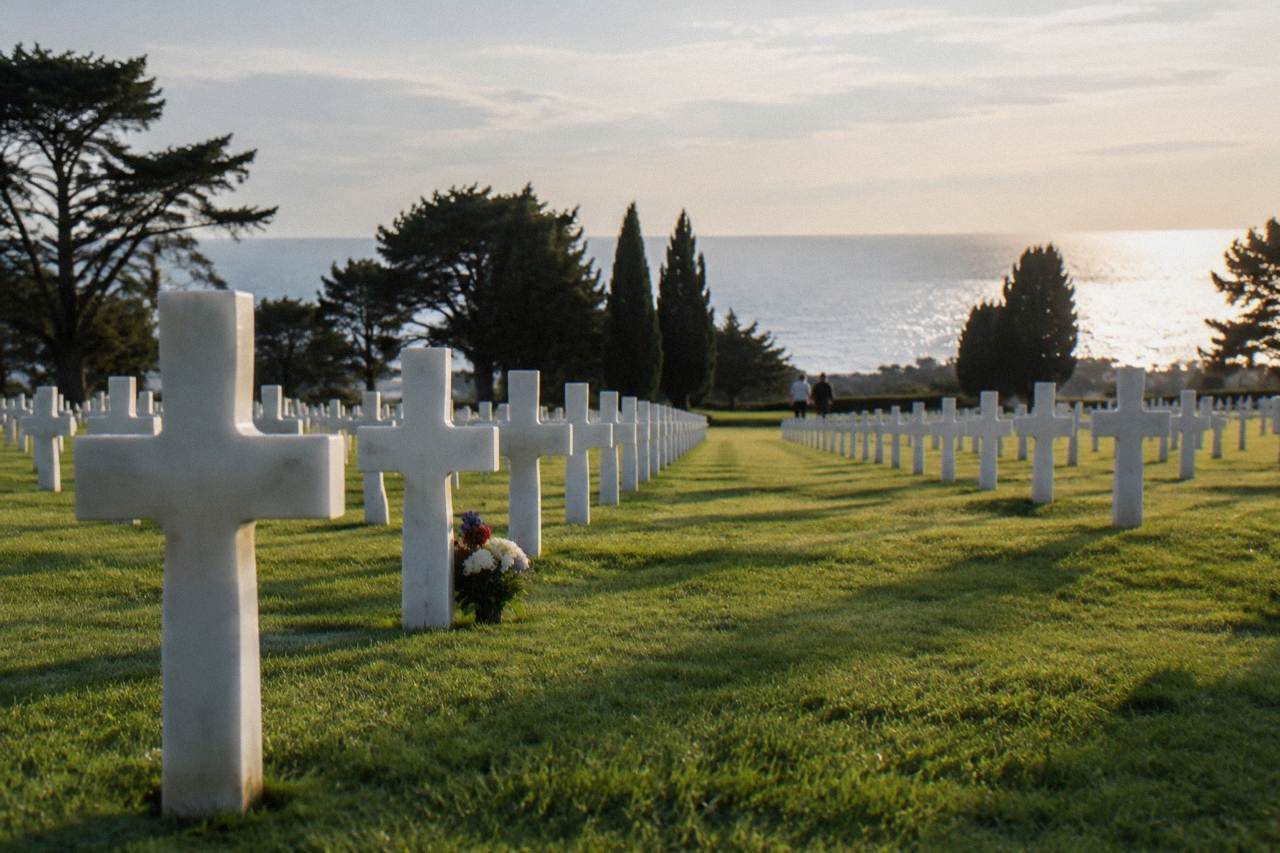 Rows of white marble headstones on a green lawn above the Normandy coastline