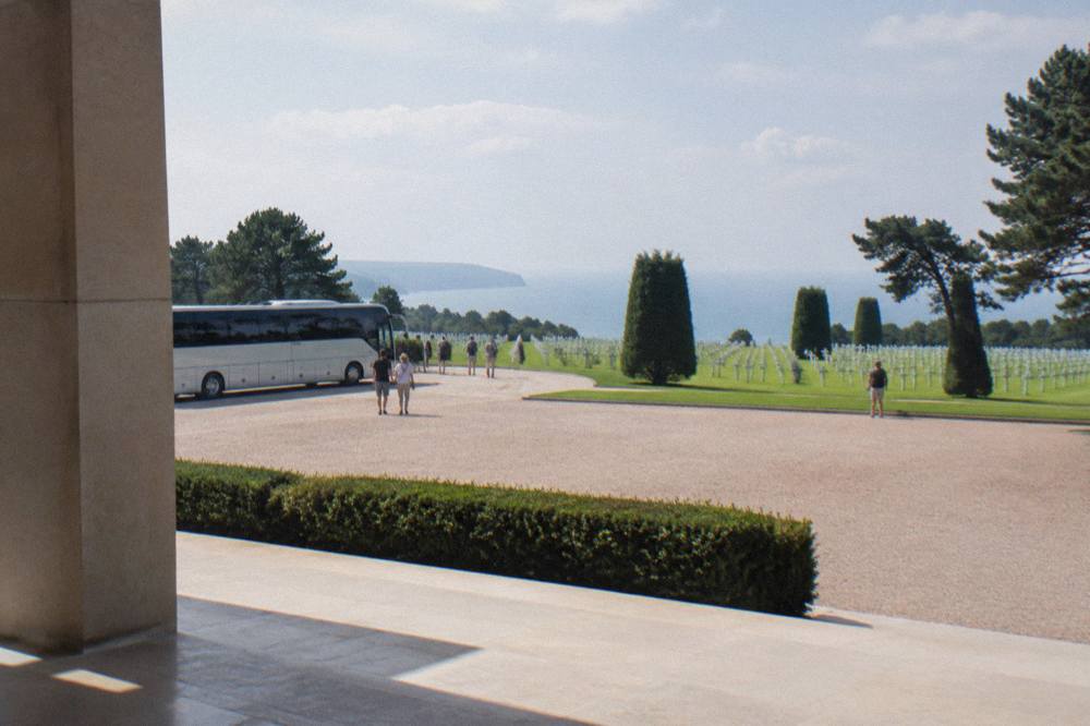 Coach parked near the esplanade of the Normandy American Cemetery with rows of white crosses beyond