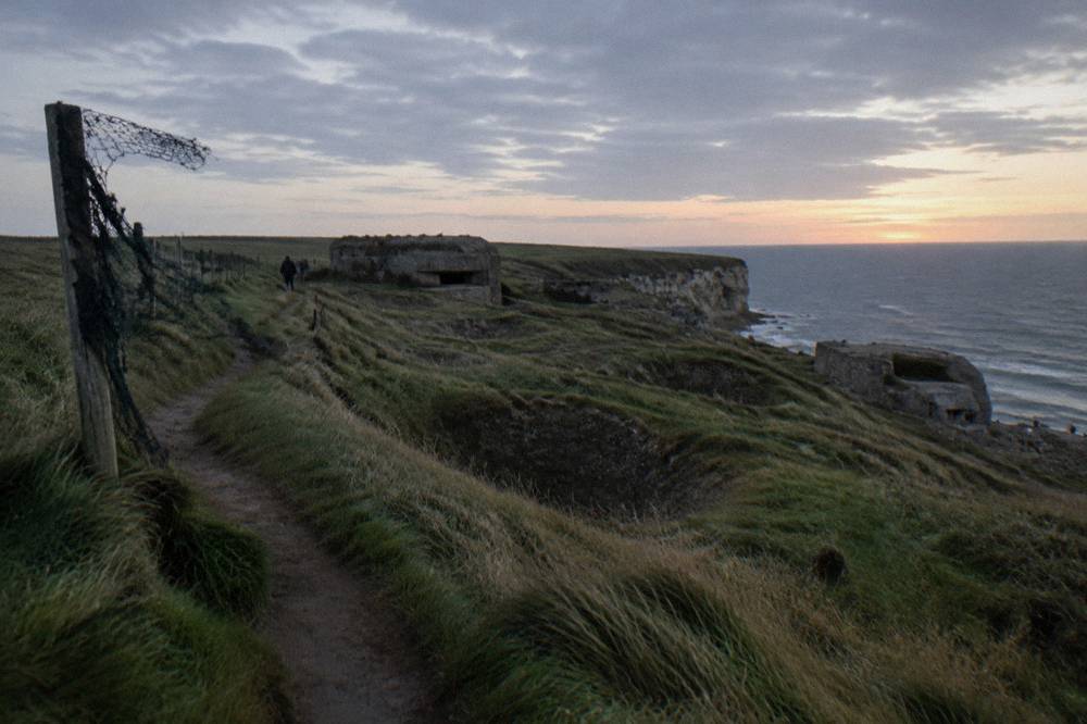 Clifftop walking path above the cratered ground at Pointe du Hoc with the sea beyond