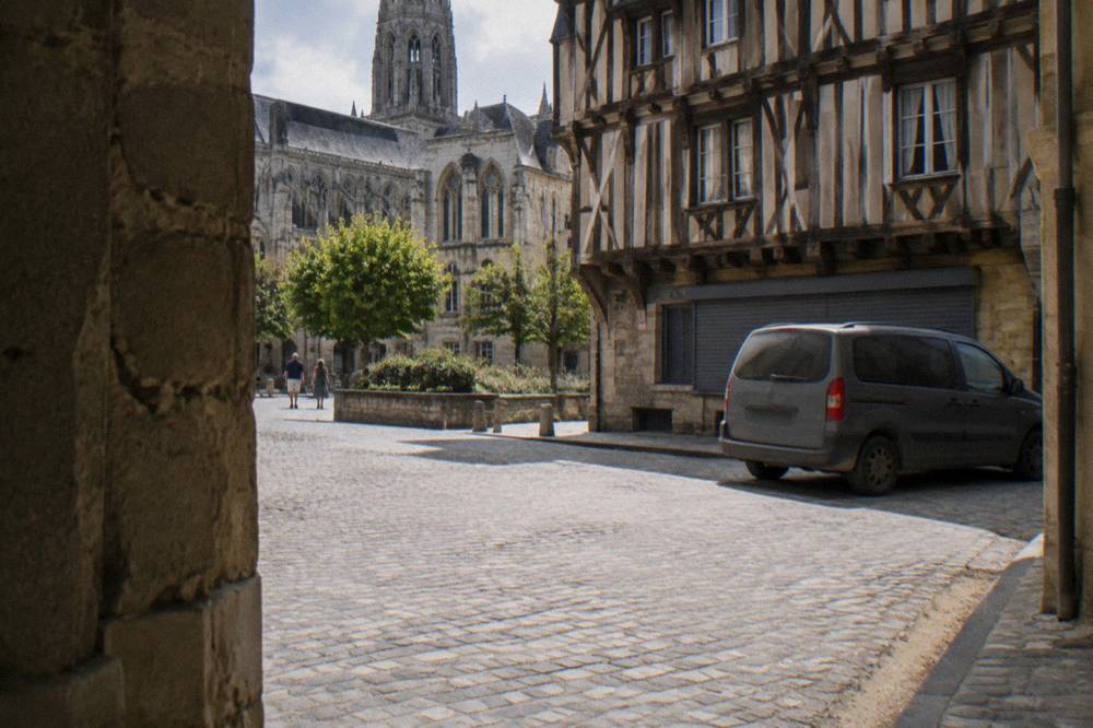Minivan waiting on a small square beside medieval half-timbered buildings in Bayeux