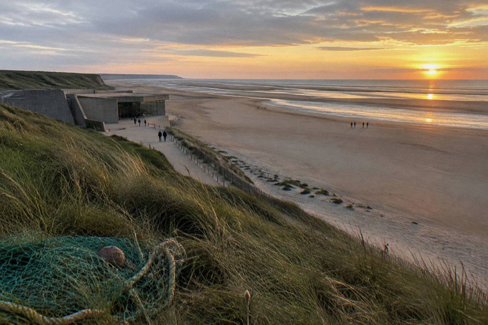 Wide sandy stretch of Utah Beach at low tide with dune grass along the dune line