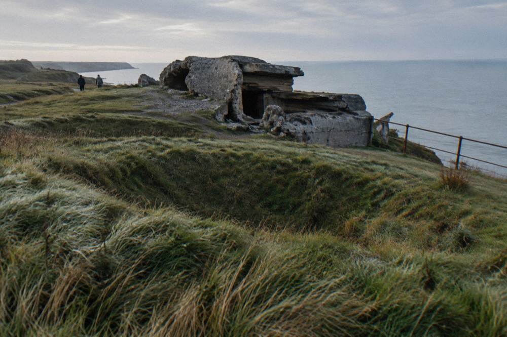 Shattered concrete bunker in cratered grass at Pointe du Hoc above the Channel