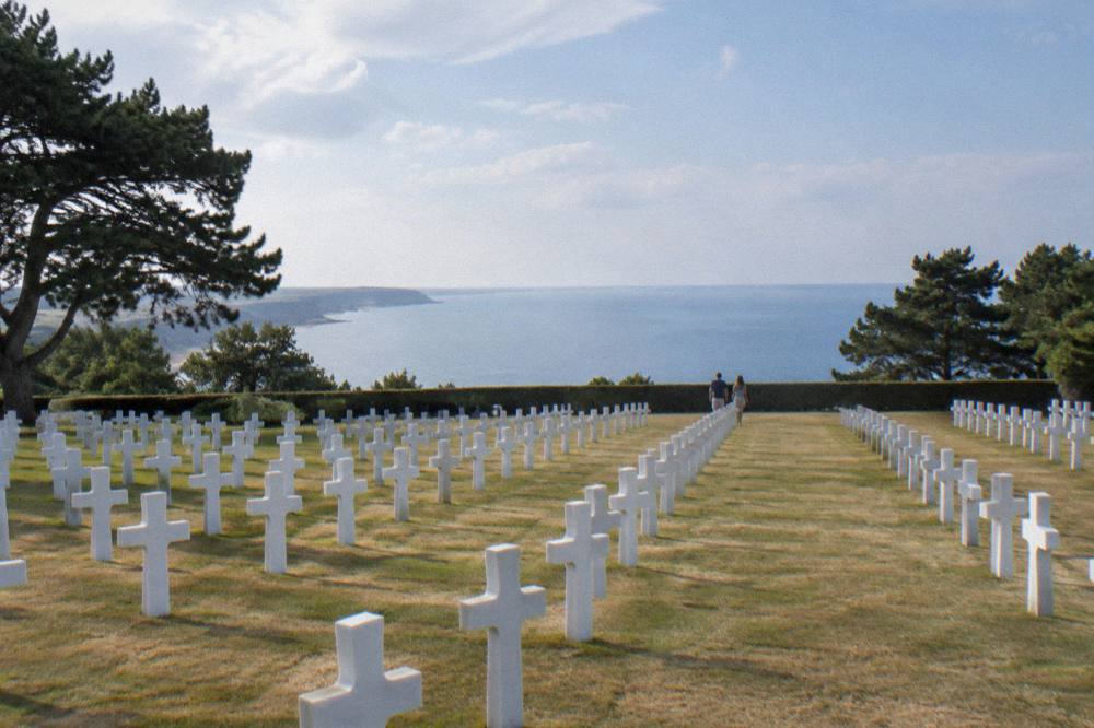 Rows of white markers in the Normandy American Cemetery with the sea beyond the bluff