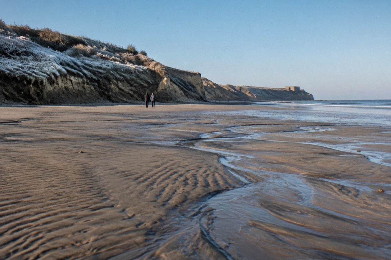 Wide view of Omaha Beach sand sloping toward the sea with grassy bluffs in the distance
